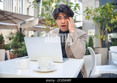 Un giovane scioccato che usa il computer portatile in un caffè all'aperto Foto Stock