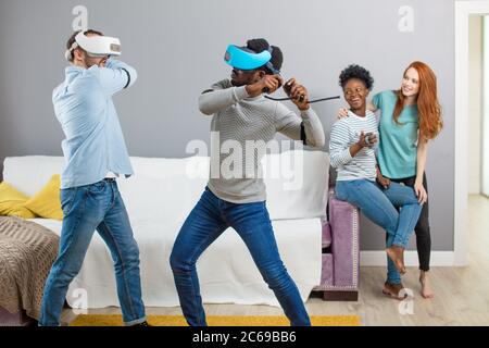 Gruppo di multirazziale maschio femmina amd gli studenti la riproduzione di gioco virtuale utilizzando occhiali VR, divertirsi insieme ay home - Virtual omg la realtà e portatile di Foto Stock