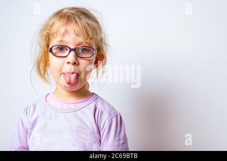 Ritratto di bambina dolce con occhiali come lei sta attaccando la lingua fuori, lingua strisciante. Foto Stock