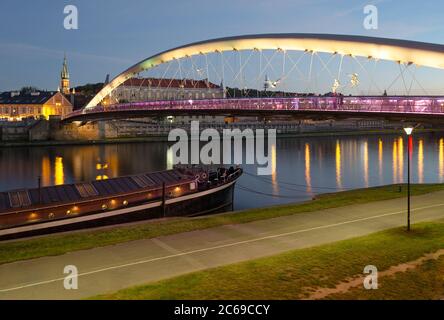 Il ponte pedonale di Padre Bernatek che attraversa il fiume Vistola con barca e sentiero sottostante a Cracovia, Polonia Foto Stock