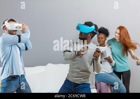 Gruppo di multirazziale maschio femmina amd gli studenti la riproduzione di gioco virtuale utilizzando occhiali VR, divertirsi insieme ay home - Virtual omg la realtà e portatile di Foto Stock