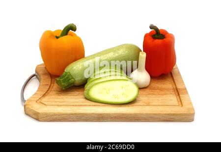 Zucchine, testa di aglio e un paio di peperoni dolci gialli e arancioni maturi su un tagliere su sfondo chiaro. Prodotto naturale. Colore naturale. Foto Stock
