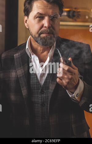 Ritratto di una bella coppia uomo caucasico in elegante abito e camicia bianca con un tubo nella sua bocca in colori caldi soggiorno, bassa luce interiore. Foto Stock