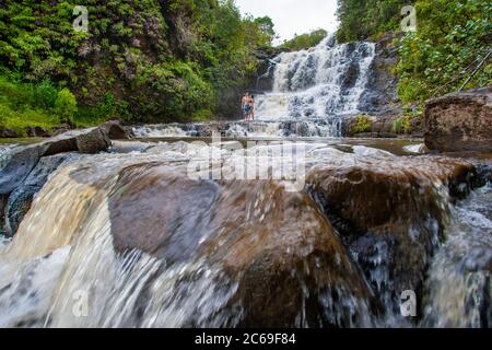 Una giovane coppia che si trova di fronte a una cascata su un terreno privato sull'isola di Kauai, Hawaii, USA. Foto Stock
