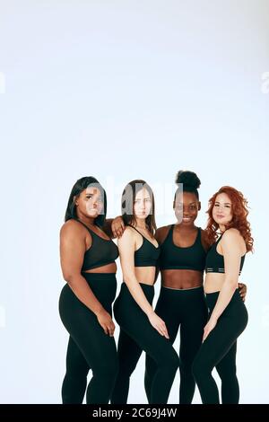 Studio ritratto di due donne caucasiche di diversa figura e dimensione che si pongono insieme in tute sportive nere contro uno sfondo grigio Foto Stock