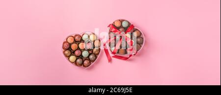 Caramelle al cioccolato tartufo fatto di cioccolato di diversi colori in una scatola a forma di cuore su sfondo rosa. Vacanza dessert Foto Stock