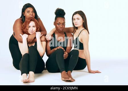 Studio ritratto di due donne caucasiche di diversa figura e dimensione che si pongono insieme in tute sportive nere contro uno sfondo grigio Foto Stock