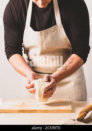 Processo concettuale di produzione di pane fatto in casa senza lievito alternativo. Un uomo impasta una pentola per impastare con l'impasto sul tavolo. Foto Stock