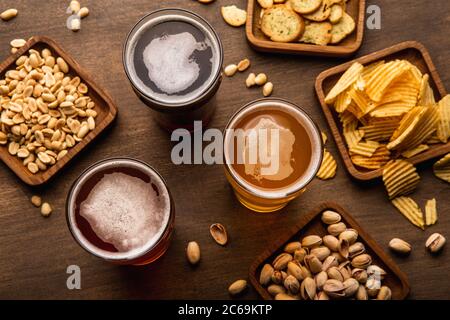 Potrete gustare bevande in bicchieri e pistacchi, noci, cracker, patatine fritte in piatto e sparse su un tavolo di legno Foto Stock