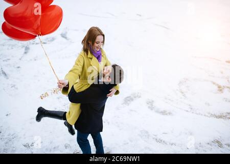felice coppia, giovane uomo e donna passare insieme romantico passatempo, a piedi in strada invernale con palloncini d'aria rossa, celebrare il loro anniversario, uomo Foto Stock