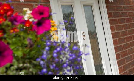 Fiori graziosi in un cestino appeso vicino all'ingresso di una casa in Inghilterra, Regno Unito. Foto Stock