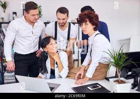 Gruppo internazionale di persone di diversa apparenza si è riunito vicino a donna asiatica mostrando nuovo progetto sul laptop, discuterne Foto Stock