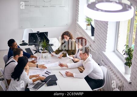 Utilizzando i laptop al lavoro, le persone che lavorano seduti al tavolo discutono di strategia, un sacco di documenti sul tavolo, la finanza Foto Stock