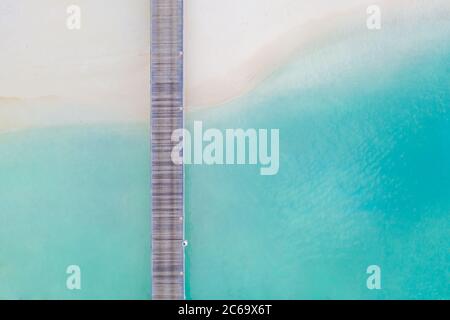 Vista aerea dall'alto di un molo di legno su una laguna oceanica azzurra e una riva tropicale sabbiosa. Paesaggio marino artistico di viaggio. Paradiso di vacanza in un resort di lusso Foto Stock