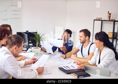 Creazione di una nuova idea aziendale da parte di un gruppo multietnico seduto in ufficio riunioni, sfondo bianco interno. Indossare abiti formali, tenere carte. Asiatico, c. Foto Stock