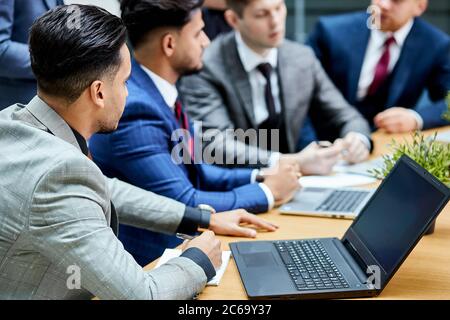 Giovani uomini riuniti per discutere nuovo progetto, utilizzare il laptop, sedersi sul tavolo, giovani uomini d'affari in ufficio con il tuxedo Foto Stock