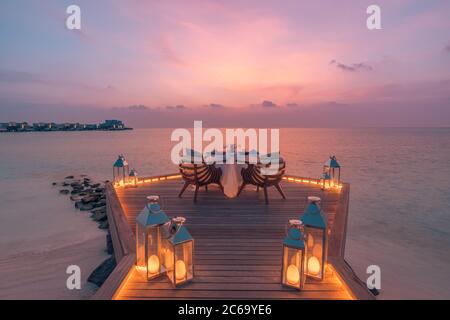 Cena romantica e lussuosa al resort tropicale al tramonto. Concetto di ristorazione esotico per destinazioni di viaggio. Candele sopra l'acqua ristorante di legno Foto Stock