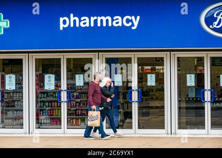 Edimburgo, Scozia, Regno Unito, 8 luglio 2020. Le maschere facciali sono la norma su Princes Street con sempre più persone che le indossano, soprattutto per andare nei negozi, anche se non diventano obbligatori nei negozi in Scozia fino a venerdì. Una coppia che indossa maschere facciali con una borsa per lo shopping di Boots farmacia che passa accanto a Boots il negozio di farmacia Foto Stock