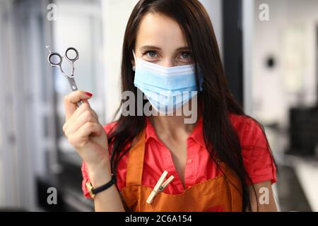 Donna parrucchiere in maschera medica tiene le forbici nelle mani. Foto Stock