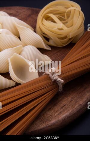 Pasta sagomata e pasta semplice. Pasta di diverse forme e colori con una varietà di frutta e piatti in legno. Foto Stock