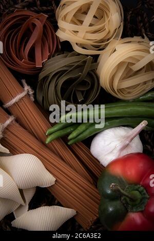 Pasta sagomata e pasta semplice. Pasta di diverse forme e colori con una varietà di frutta e piatti in legno. Foto Stock