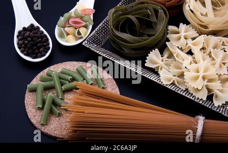 Pasta lunga marrone e pasta sagomata e pasta colorata in un recipiente e pepe nero. Foto Stock