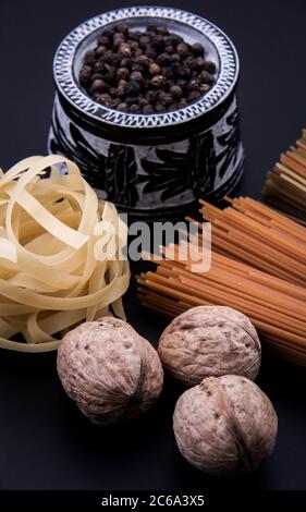 Pasta lunga di colore marrone con pasta sagomata e una ciotola di pepe nero e alcune noci insieme. Foto Stock