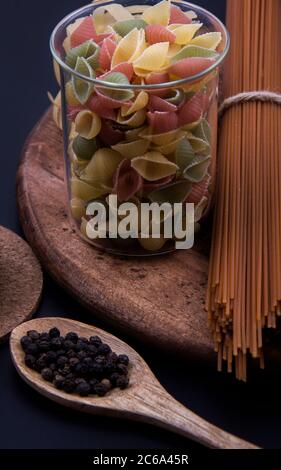 Pasta lunga marrone e pasta colorata di diverse misure con una ciotola di pepe nero. Foto Stock