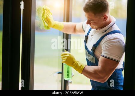 Il servizio di pulizia è arrivato a pulire la nuova casa. Uomo caucasico duro pulire accuratamente il finestrino. Vista laterale Foto Stock