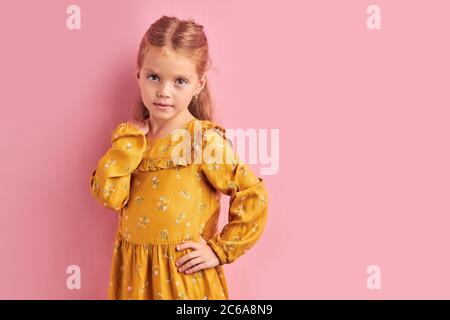 Ragazza carina e bella piccola in vestito giallo guardare fotocamera in posa. Sfondo rosa isolato Foto Stock