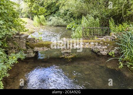 Un piccolo ponte di pietra clapper sul fiume Windrush infant come scorre attraverso il villaggio Cotswold di Naunton, Gloucestershire UK Foto Stock