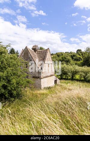 Un vecchio colombino di pietra (c.1600 DC) accanto al fiume infante Windrush come scorre attraverso il villaggio di Cotswold di Naunton, Gloucestershire UK Foto Stock