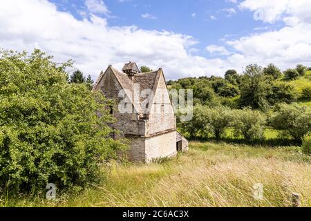 Un vecchio colombino di pietra (c.1600 DC) accanto al fiume infante Windrush come scorre attraverso il villaggio di Cotswold di Naunton, Gloucestershire UK Foto Stock