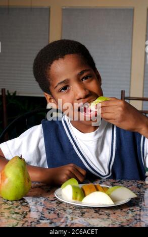 Austin, Texas USA, dicembre 2003: Un ragazzo afro-americano di otto anni che mangia una pera a casa. SIGNOR ©Bob Daemmrich Foto Stock