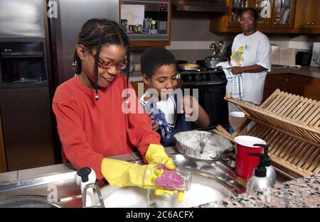 Austin, Texas USA, dicembre 2003: La ragazza afro-americana (10) e il fratello (8) lavano i piatti a casa mentre la madre guarda. Modello rilasciato. ©Bob Daemmrich Foto Stock