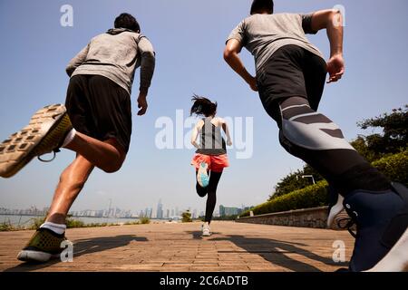 tre giovani adulti asiatici che corrono all'aperto, vista posteriore e ad angolo basso Foto Stock