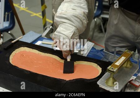 Houston Texas USA, 16 settembre 2003: Durante un tour stampa al Johnson Space Center, un tecnico della NASA che indossa guanti per tute spaziali dimostra l'uso del riempitivo in plastica epossidico che verrà utilizzato per riparare le piastrelle danneggiate dello Space Shuttle dagli astronauti nello spazio. ©Bob Daemmrich Foto Stock