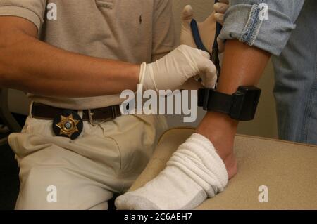 Austin, Texas USA, 5 settembre 2003: L'agente della libertà vigilata del Texas collega un dispositivo di monitoraggio elettronico alla caviglia di un parolee. ©Bob Daemmrich Foto Stock