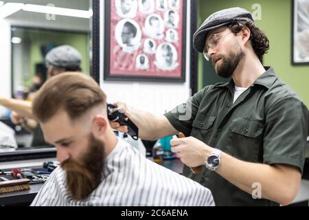 Le mani del giovane barbiere rendendo scarti da uomo attraente in Barberia Foto Stock