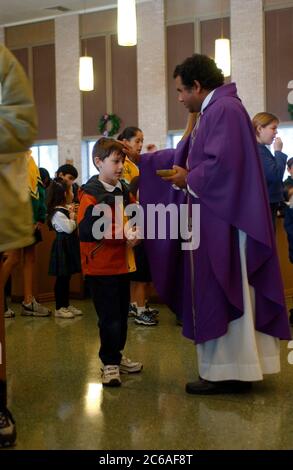 Austin, Texas USA, dicembre 2003: Il sacerdote indiano in visita dà la comunione in messa per gli scolari a St. Ignatius Martyr Catholic Parish a Natale. ©Bob Daemmrich Foto Stock