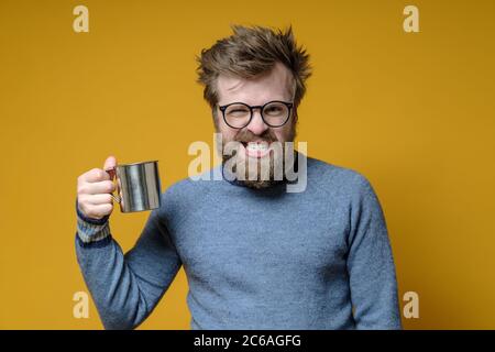 L'uomo è sconvolto e stressato, tiene in mano una tazza di metallo ed è arrabbiato che non va in escursione. Foto Stock