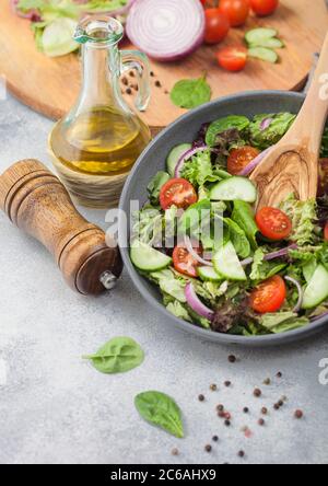 Ciotola grigia di verdure fresche salutari insalata con pomodori e cetrioli, lattuga e spinaci su sfondo chiaro con olio d'oliva, mulino e fr Foto Stock