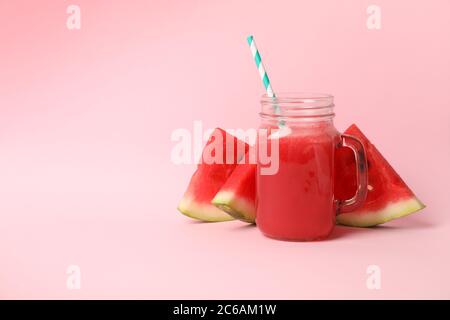 Vasetto di vetro con succo di anguria e fette su sfondo rosa Foto Stock