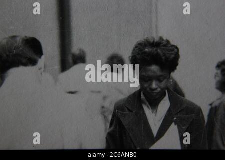 Fine anni '70 vintage nero e bianco stile di vita fotografia di una donna afroamericana che cammina nella folla. Foto Stock