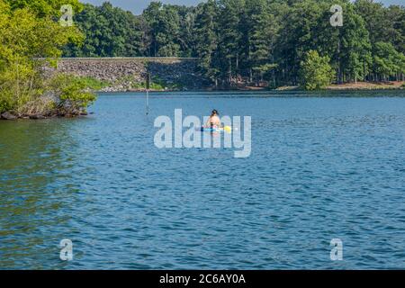 Una giovane donna che kayak lasciando il suo cane andare per una nuotata nel lago in un pomeriggio caldo in estate Foto Stock