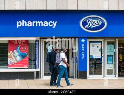 Un gruppo di uomini neri che indossano maschere facciali passa accanto al negozio Boots The Chemist durante la pandemia, Princes Street, Edimburgo, Scozia, Regno Unito Foto Stock