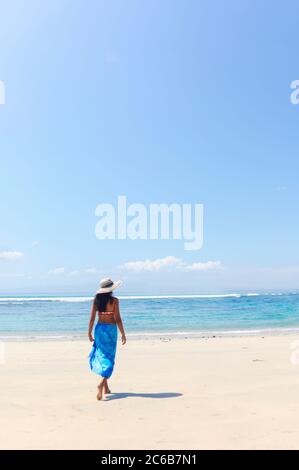 Una giovane donna in un cappello e scialle che cammina lungo una spiaggia tropicale incontaminata sull'isola di Bali, Indonesia, Sud-Est asiatico, Asia Foto Stock