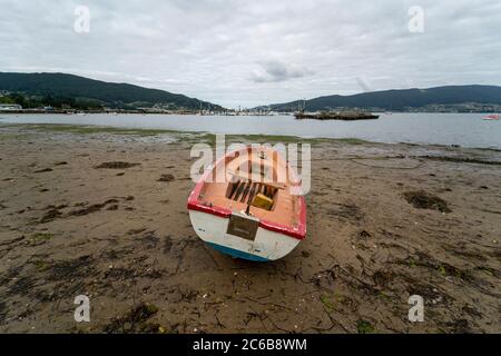 Piccola barca a remi in legno intrecciata su una spiaggia in basso marea Foto Stock