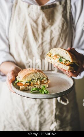 Donna che tiene fresco prima colazione sandwich con pesce fritto, limone, rucola Foto Stock