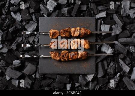 kebab sugli spiedini. Tre porzioni di carne alla griglia su un piatto di pietra. Carbone di sfondo. Vista dall'alto. Foto Stock